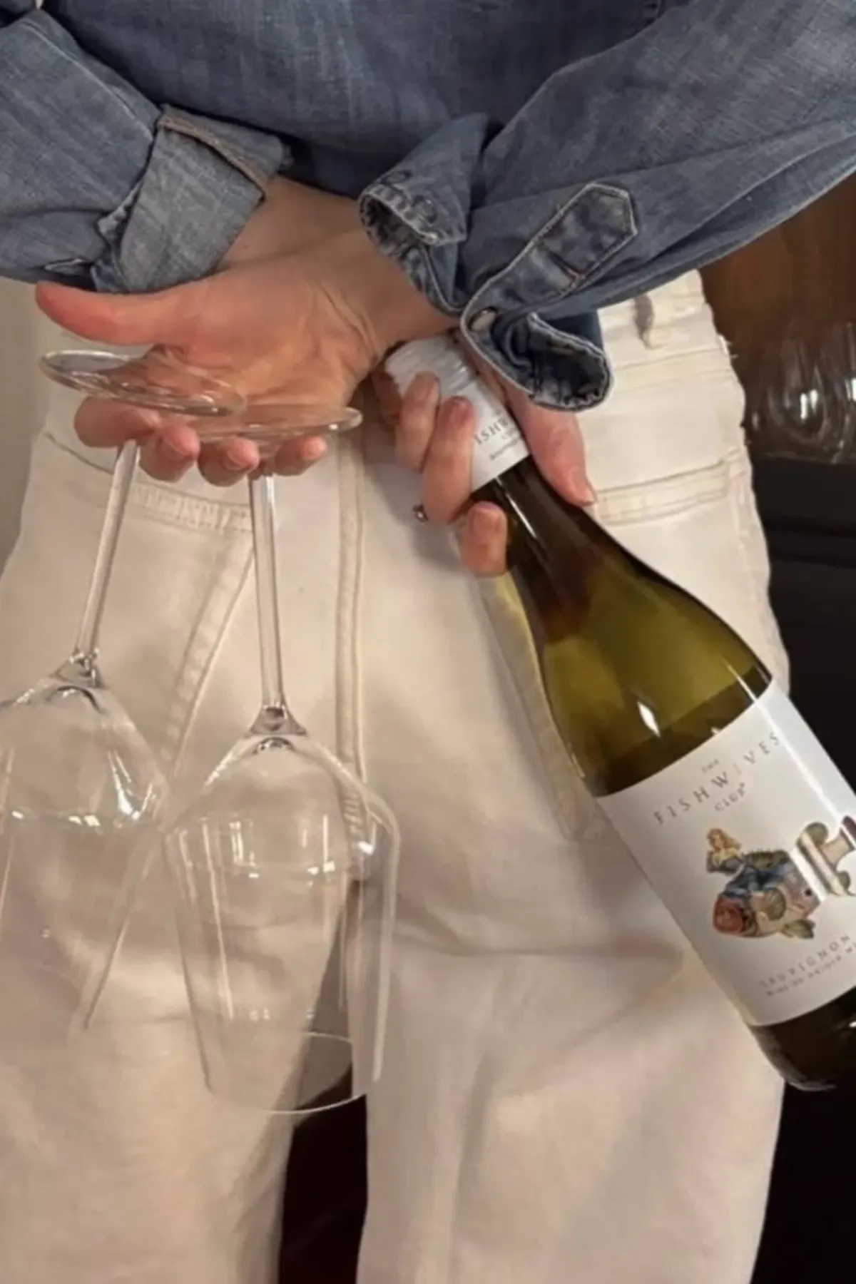 A person carrying a Fishwives bottle and two wine glasses